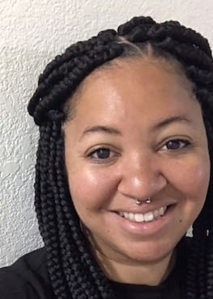 Woman with box braids and septum ring smiles at the camera.