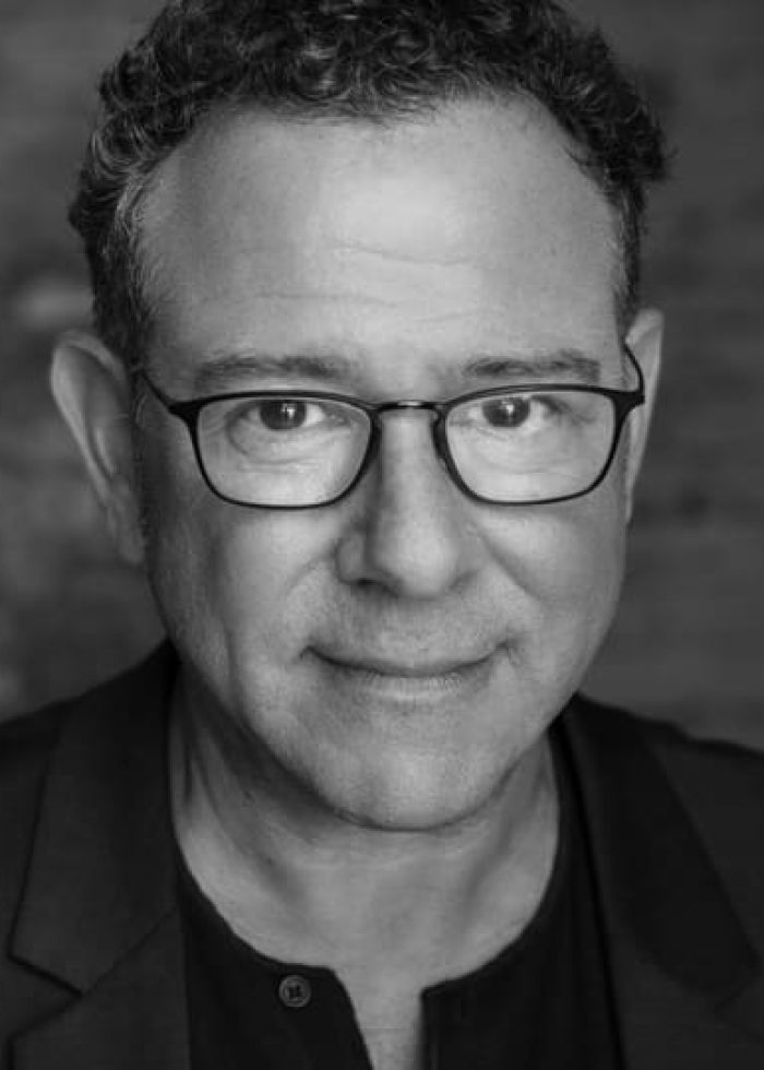 Michael Greif in a black and white headshot, wearing glasses and a blazer.
