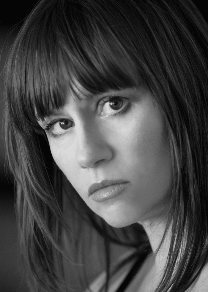 Woman with dark hair and bangs, looking intently at the camera