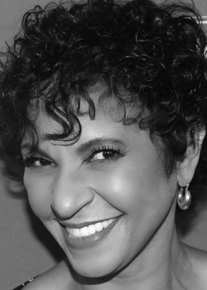 Nancy Ticotin smiling with curly hair and hoop earrings