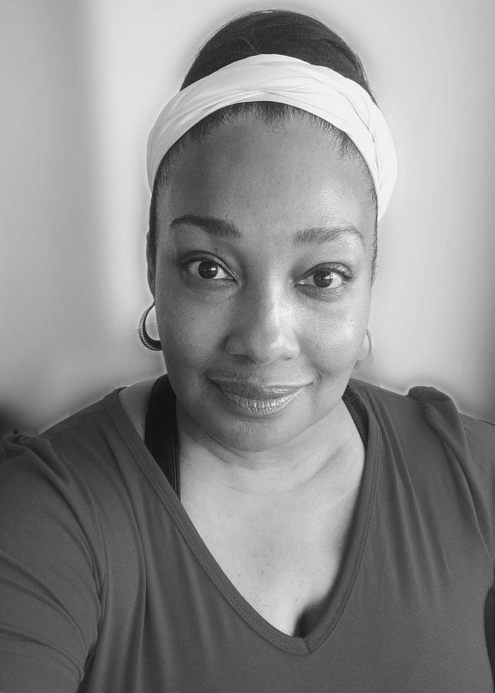 Natalie Venetia Belcon smiles, wearing a white headband and hoop earrings