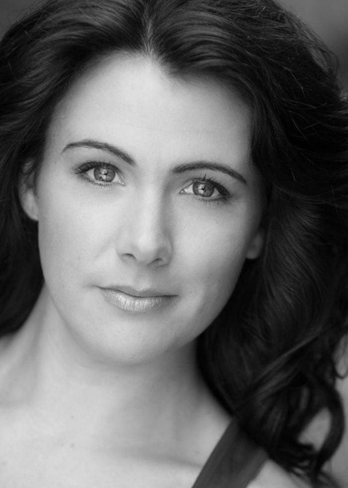 Close-up portrait of Natalie Charle Ellis with dark wavy hair, looking at the camera.