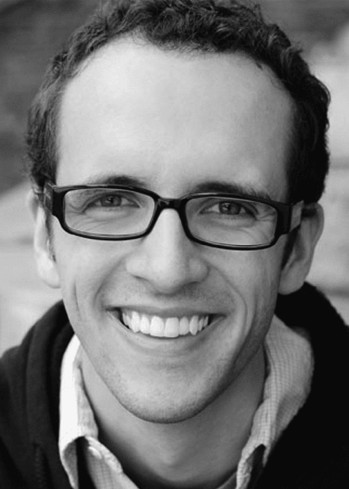 Nathan Dame smiling, wearing glasses, in a black and white headshot.