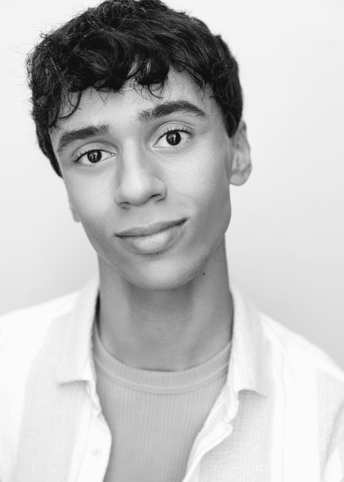 Young man with dark curly hair smiling, wearing a light shirt.