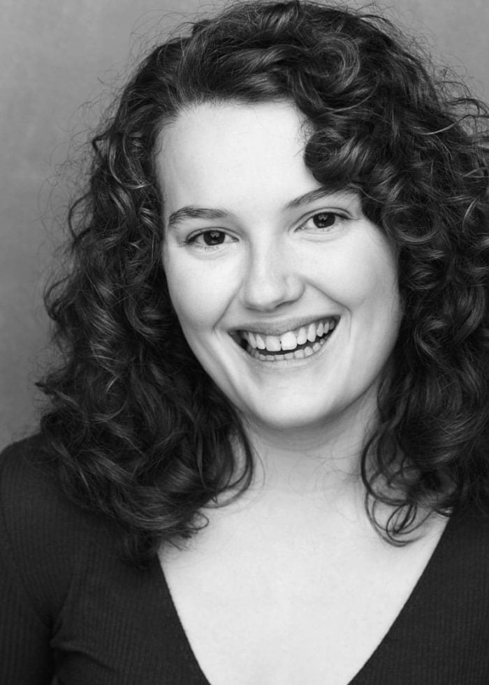 Nina White smiling in a black and white headshot with curly hair.