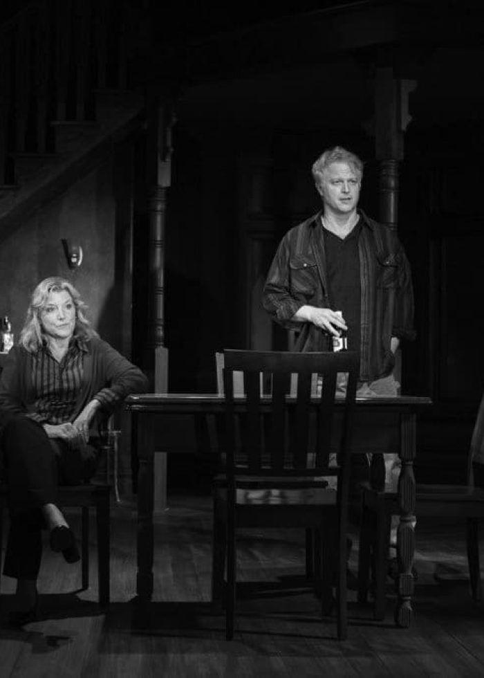 Two actors in a stage production of "On the Shore of the Wide World" in a dimly lit room.