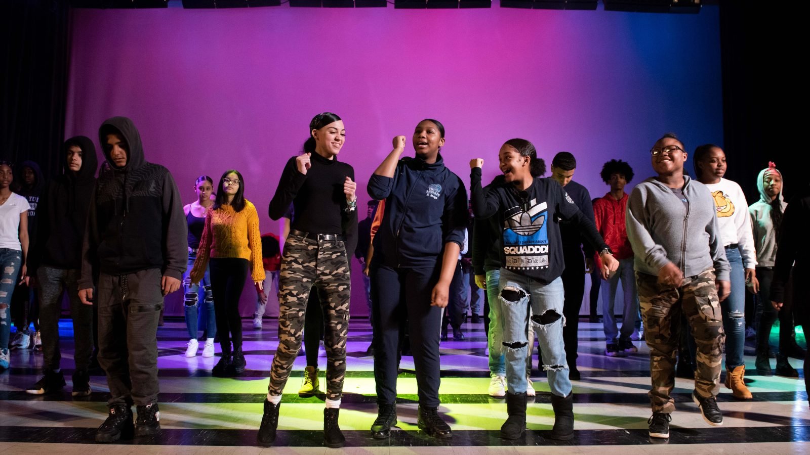 Group of young people performing on stage under colorful lights.