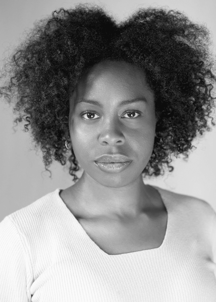 Black and white headshot of Paige Gilbert with curly hair, looking directly at the camera.