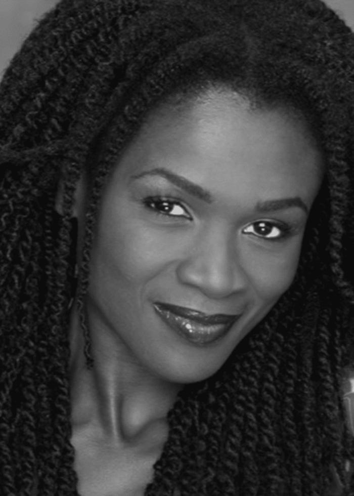 Patrice Johnson Chevannes smiling, with long braided hair and dark lipstick.
