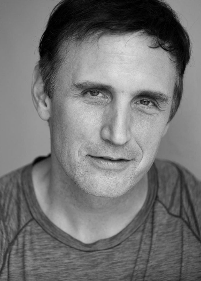 Close-up portrait of Pete Simpson, smiling, in a grey t-shirt.