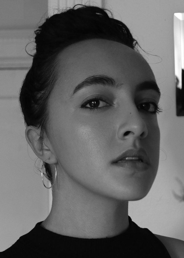 Woman with dark hair in a bun, wearing hoop earrings, looking directly at the camera.