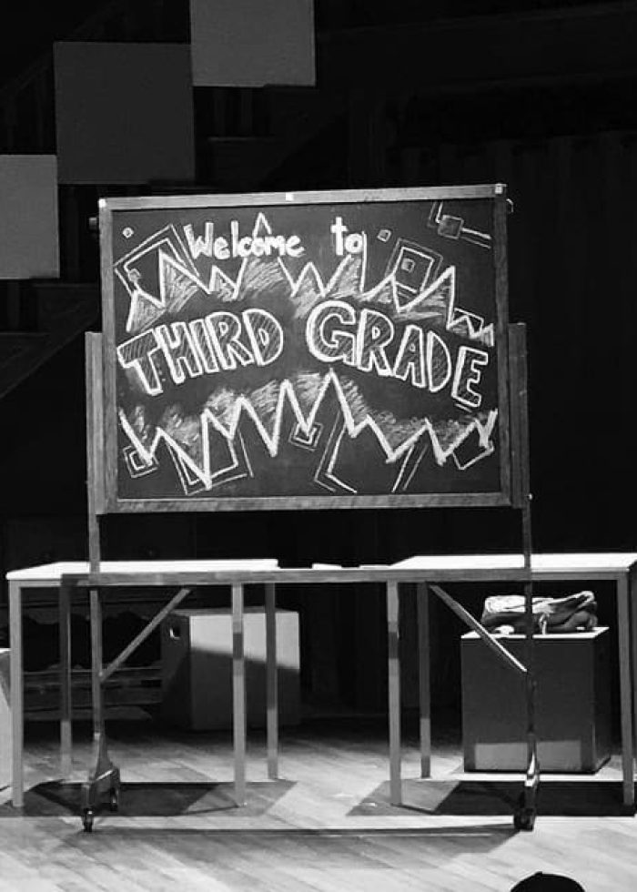 Chalkboard sign welcomes you to Third Grade. Set design for a school musical.