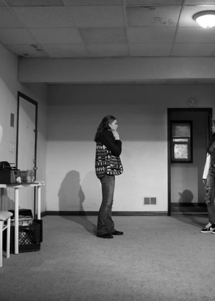 Black and white photo of a room with several people, perhaps from "The Purple Lights of Joppa Illinois’ Revels in Unease".