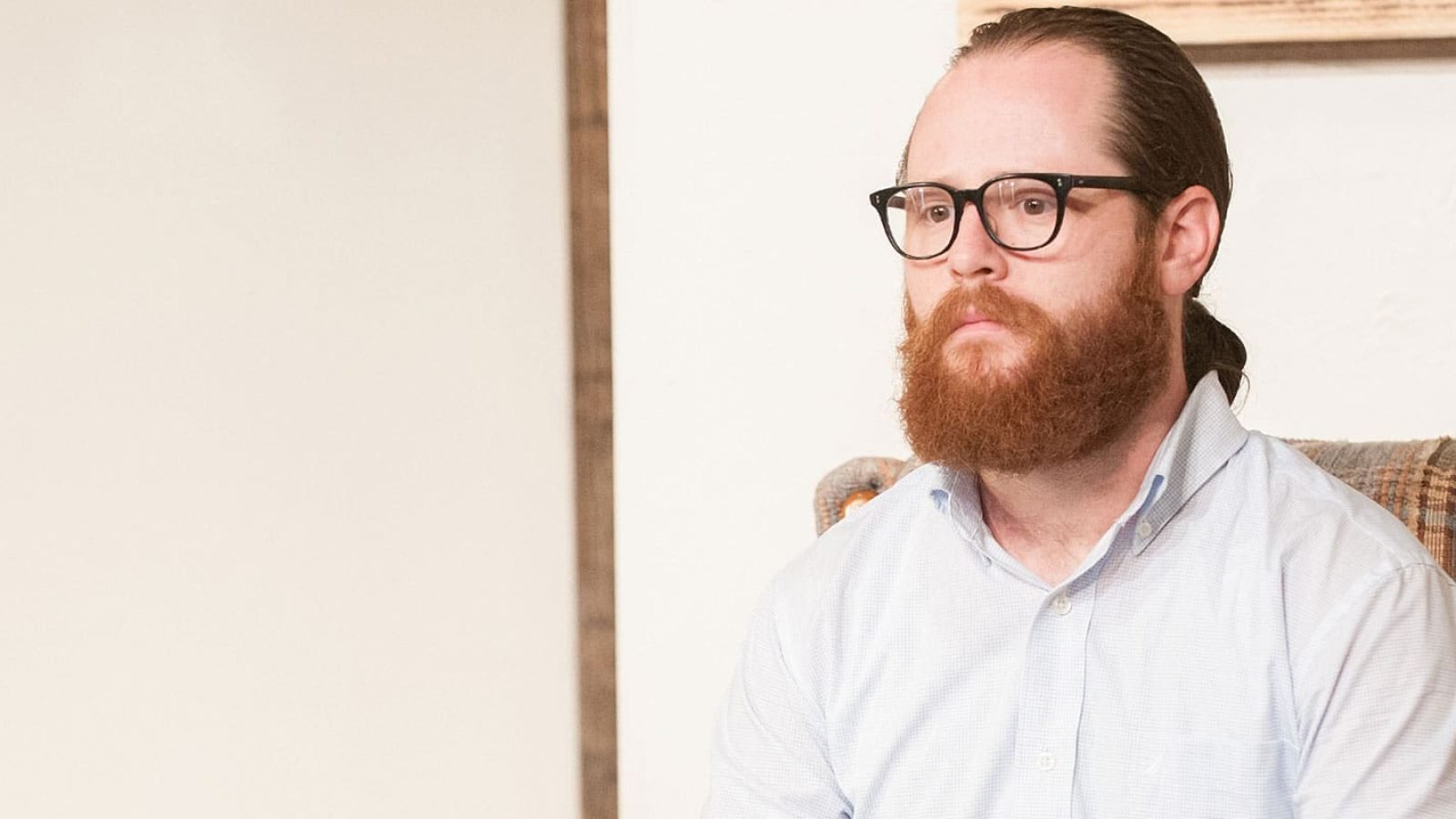 Man with glasses and beard sits in a plaid chair.