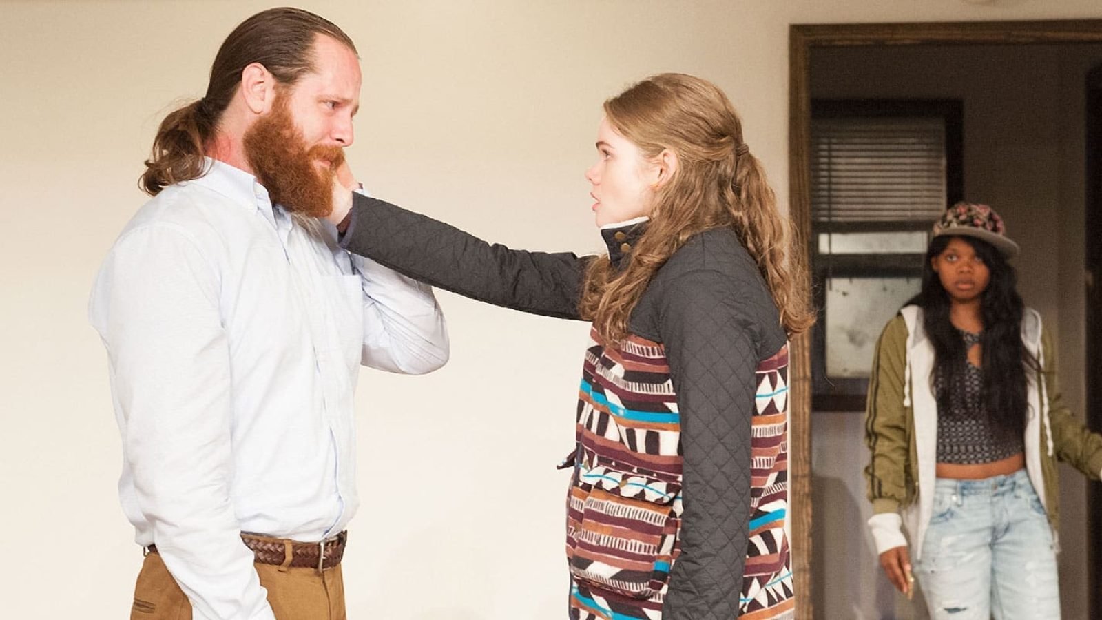 Three people in a tense scene; a man and woman face each other, while a third person looks on.