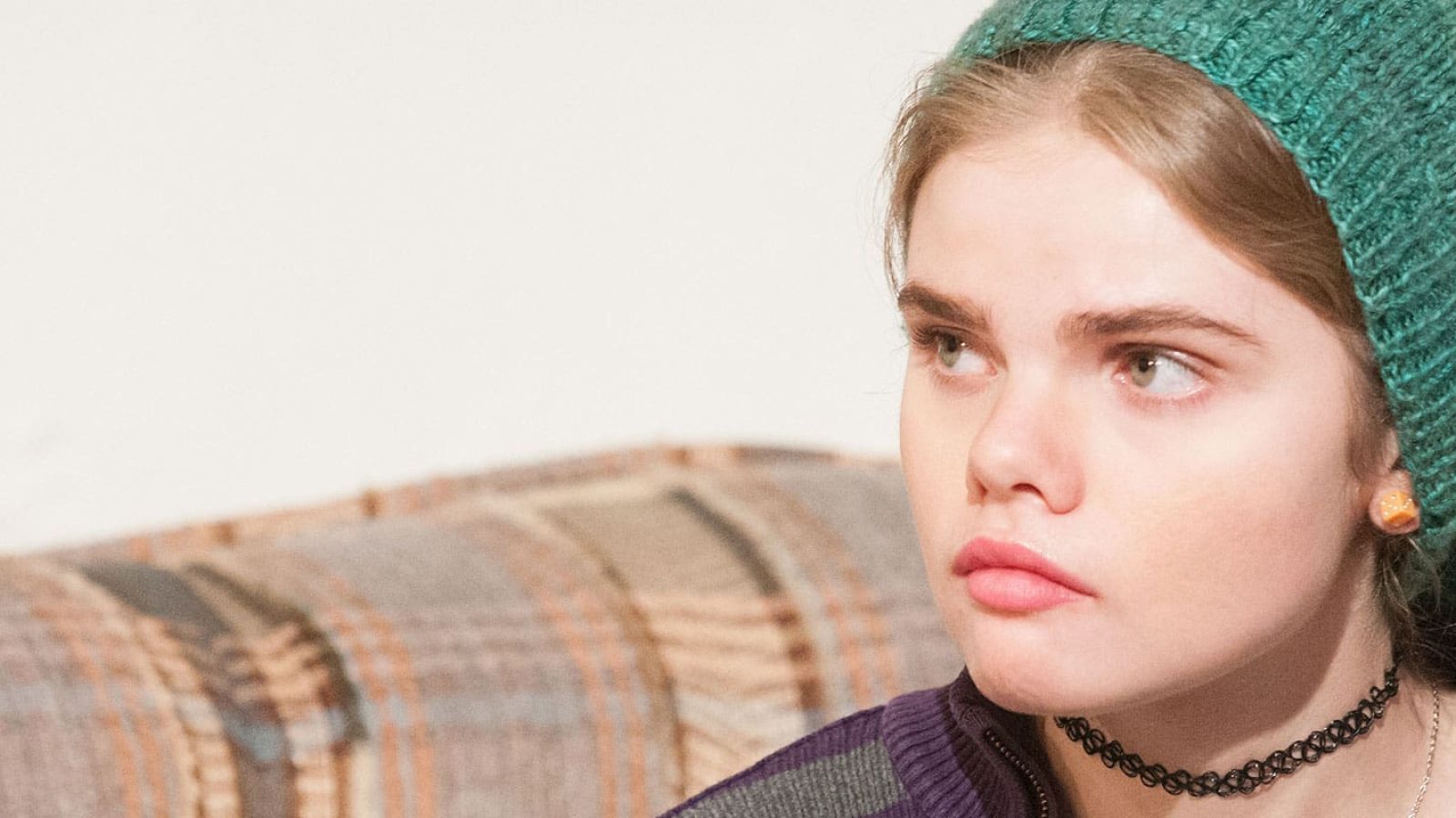 Teenage girl wearing a teal beanie, looking thoughtfully.
