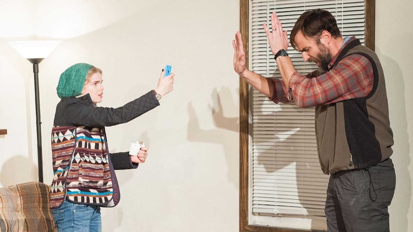 A young woman takes a selfie while a man shields his face from the camera.
