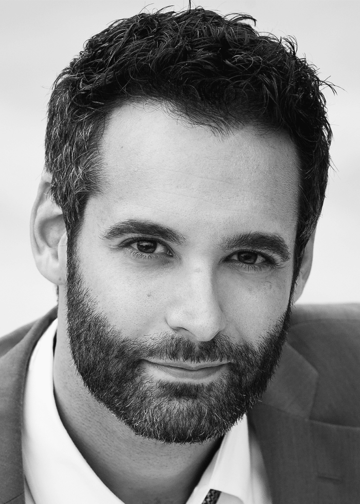 Headshot of a man with a beard wearing a suit and white shirt, looking at the camera.