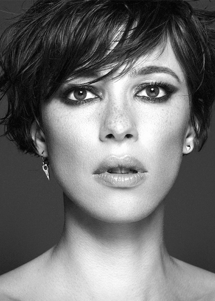 Close-up portrait of Rebecca Hall with short, dark hair and striking eye makeup.