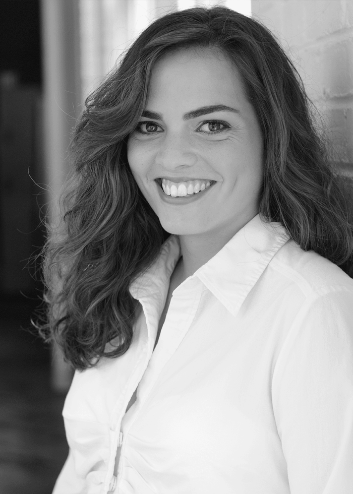 Iraisa Ann Reilly smiles, leaning against a brick wall.