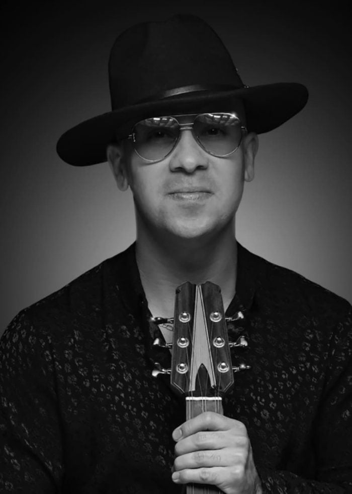 Renesito Avich holding a guitar, wearing a hat and sunglasses