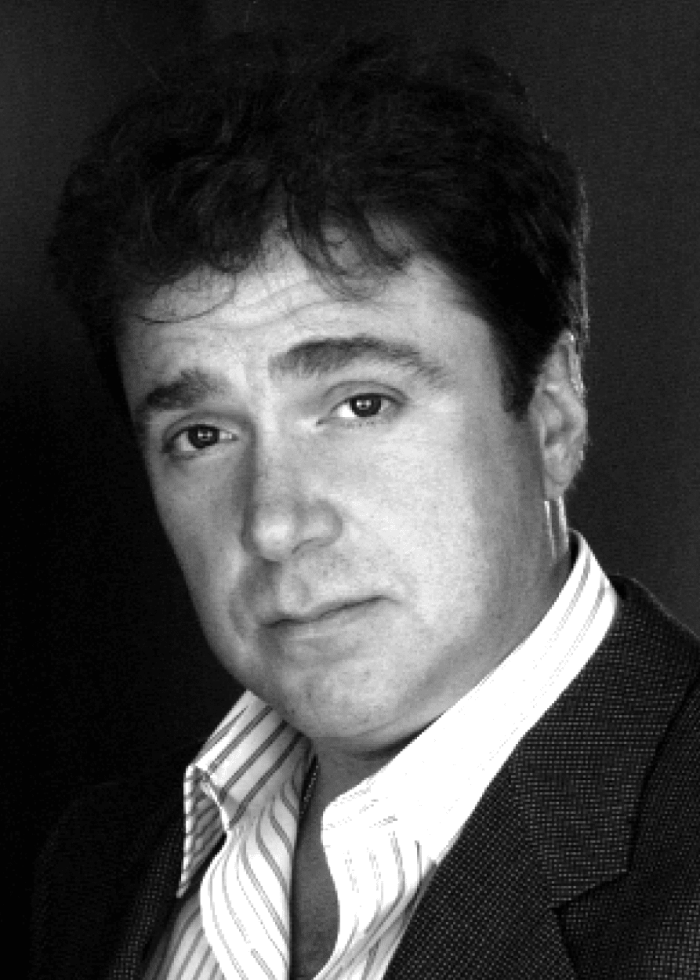 Michael Rispoli, actor, in a black and white headshot, wearing a suit jacket and striped shirt.