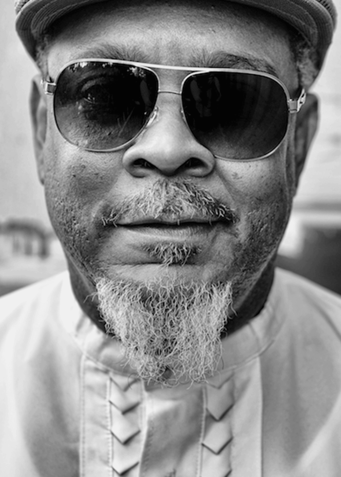 Close-up portrait of a man with sunglasses, a graying goatee, and a cap.