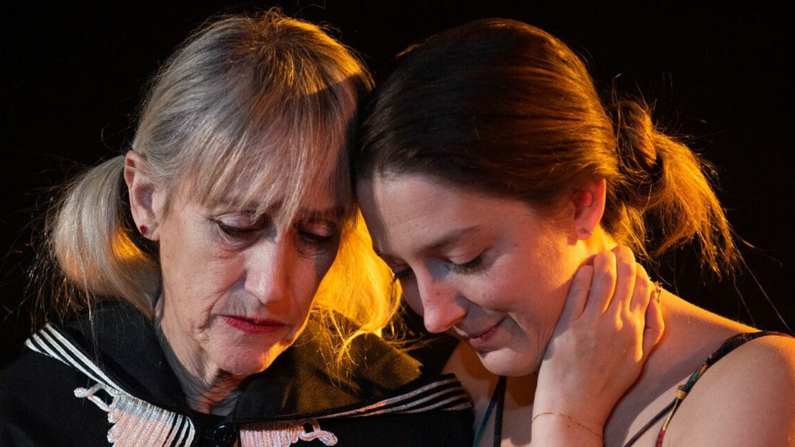 Two women embrace, heads bowed, sharing a quiet moment.