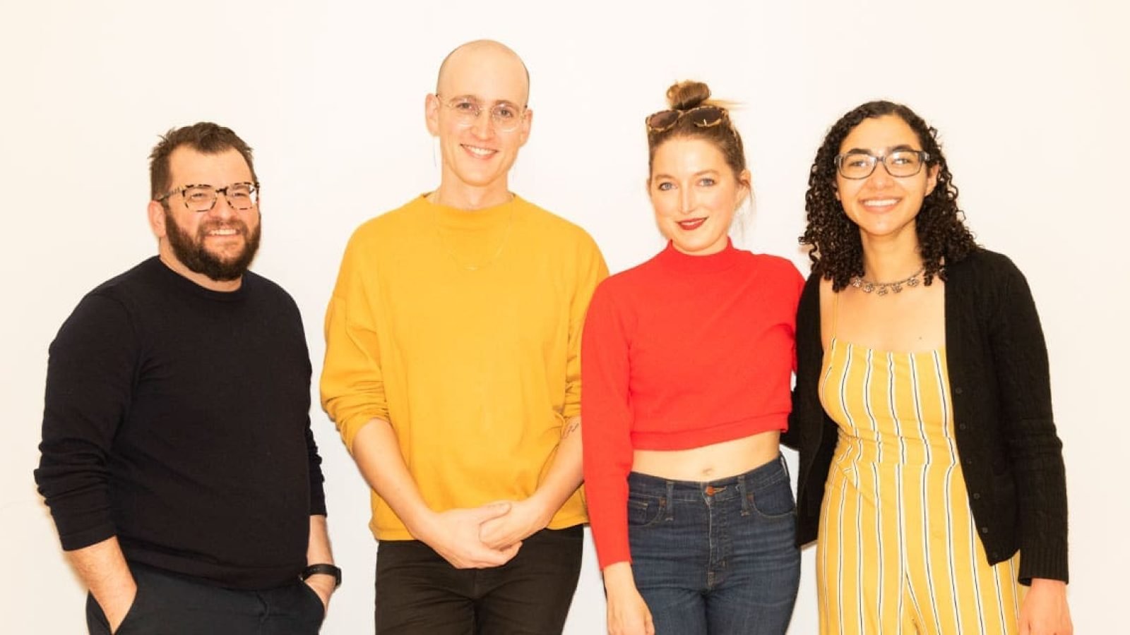 Four smiling people, two women and two men, pose against a white background.