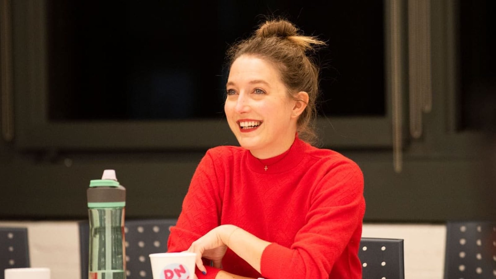 Smiling woman in red sweater, seated at a table.