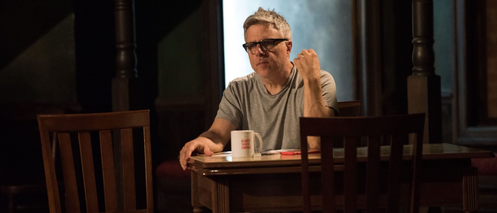 Man sitting at a table, looking thoughtful. A coffee mug and papers are visible.