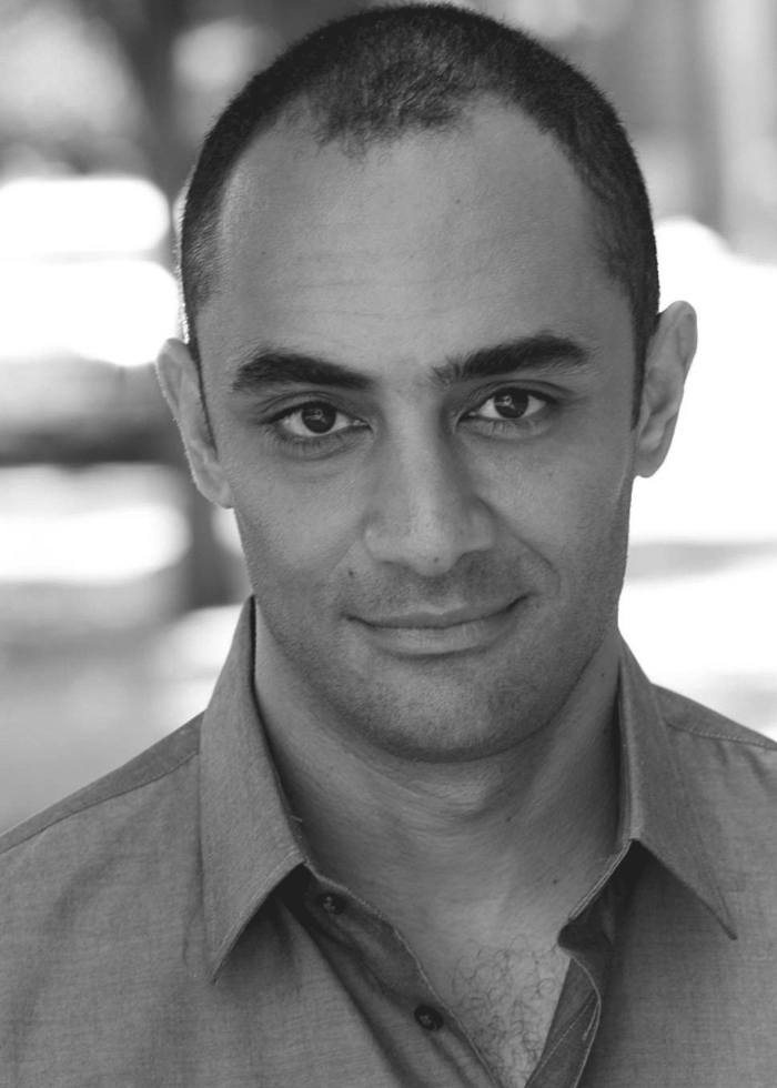 Saheem Ali, in a black and white headshot, smiling at the camera.