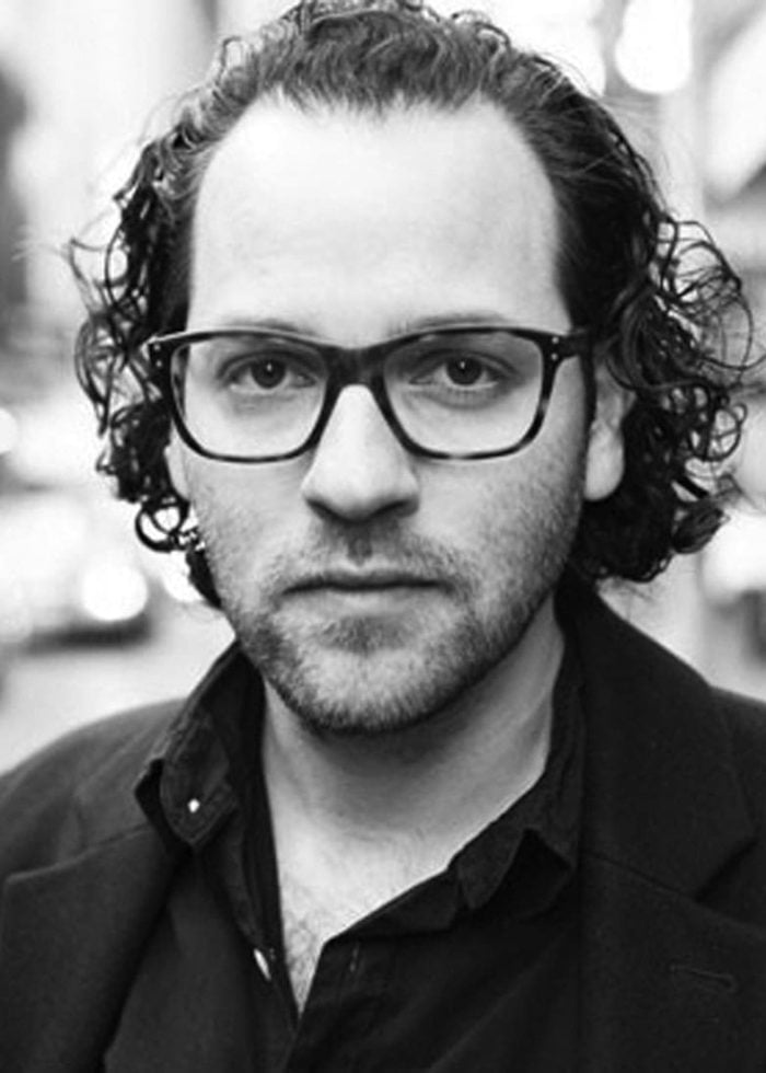 Sam Gold, a man with curly hair and glasses, looking at the camera