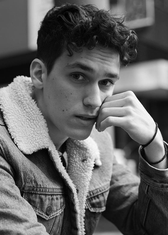 Sam Vartholomeos in denim jacket, looking thoughtful