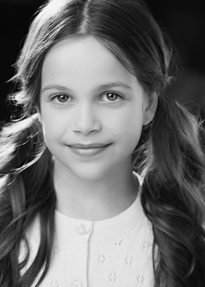 Young girl with long hair in pigtails smiles for the camera.