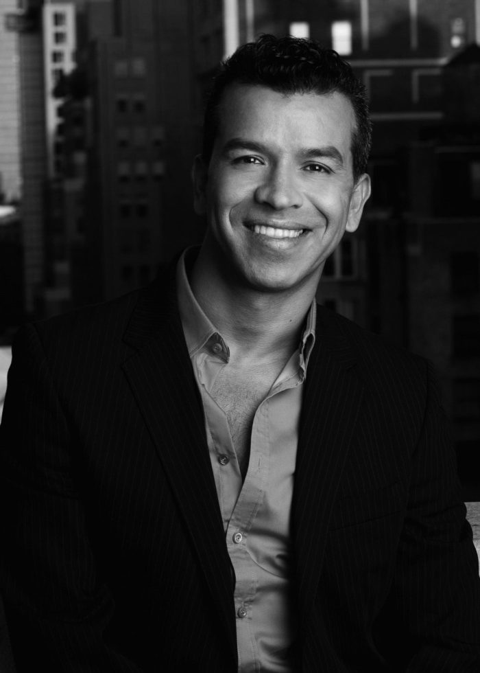 Sergio Trujillo smiling in a suit, with a city backdrop.