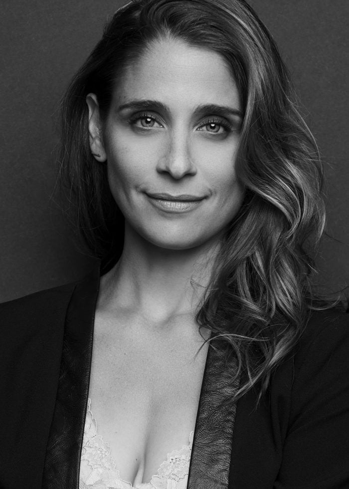 Elena Shaddow, a woman with wavy hair, smiles for the camera in a black and white portrait.