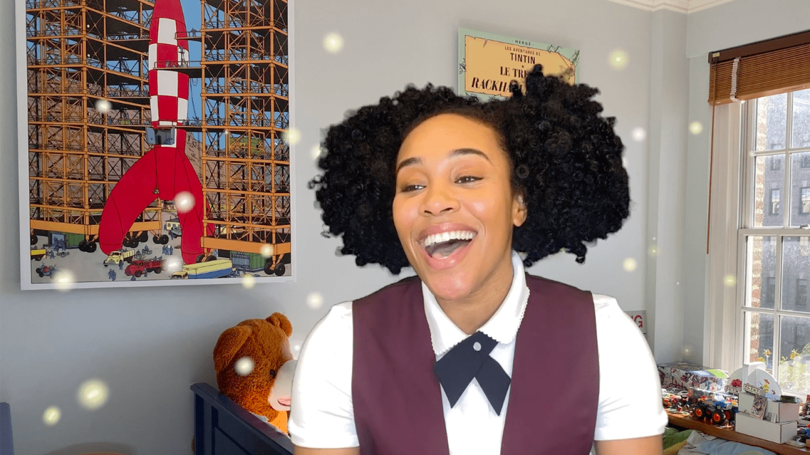 Joyful woman with curly hair laughs, wearing a maroon vest and white collared shirt. "She Persisted" musical production.