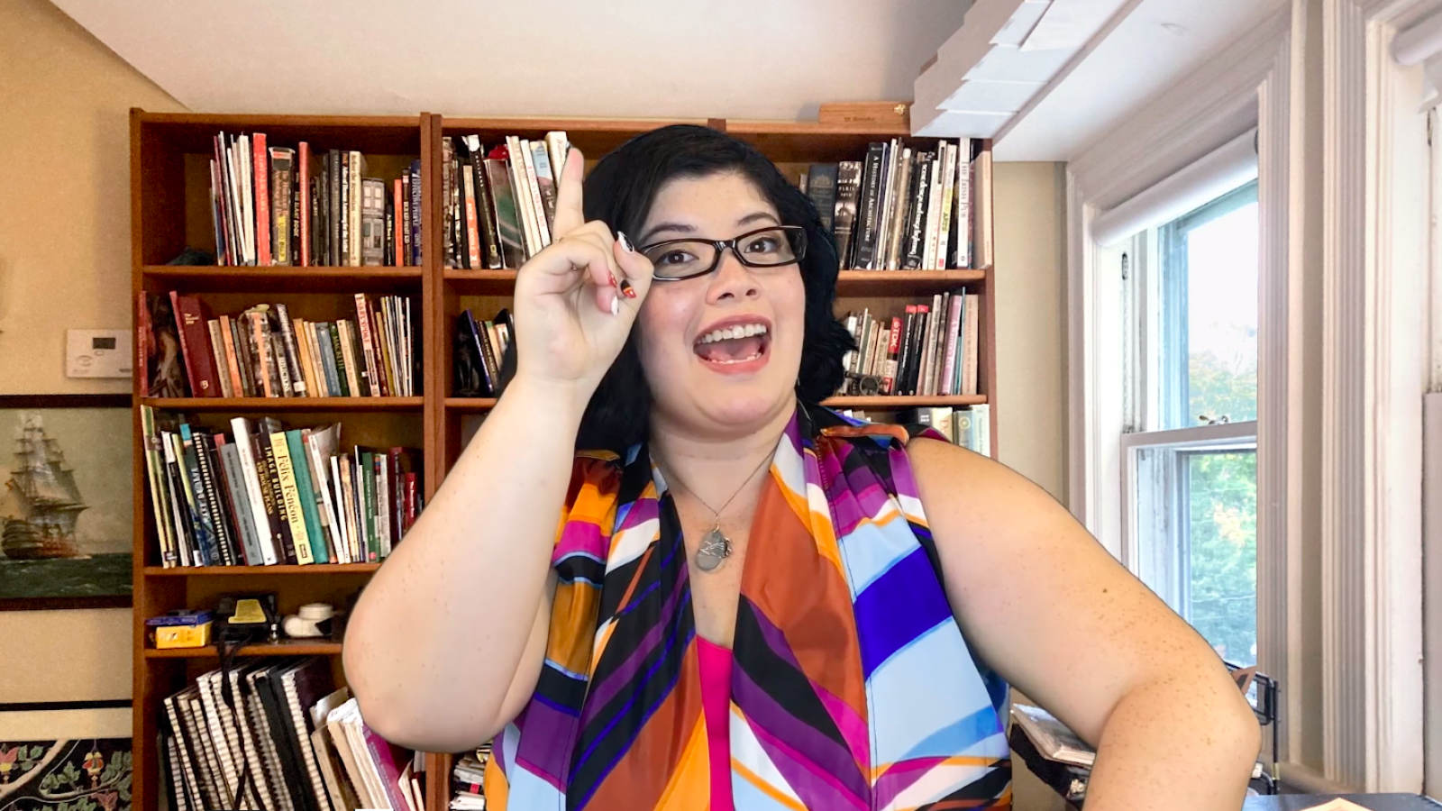 Woman in glasses making a point, "She Persisted" backdrop
