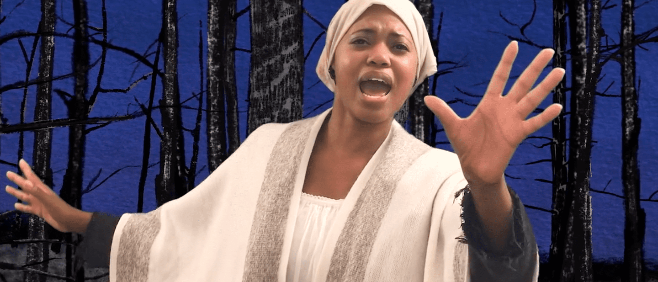 A woman in a white robe sings in a virtual production of *She Persisted, The Musical*.