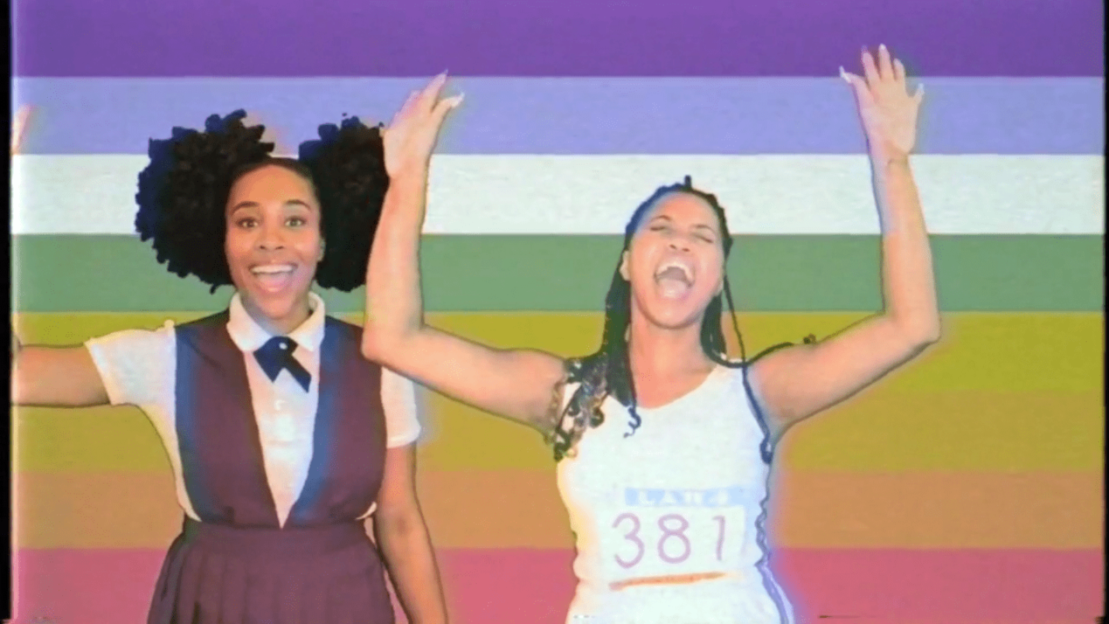 Two joyful girls celebrate; one in a school uniform, the other wearing a race bib #381. She Persisted musical.