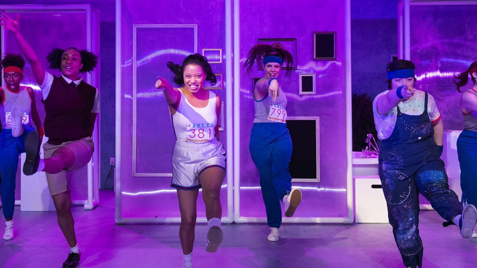 Cast of "She Persisted," the musical, in dynamic poses. Race numbers visible.