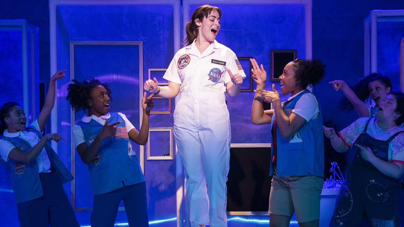Cast of She Persisted, The Musical, in a vibrant scene. Sally Ride patch visible.