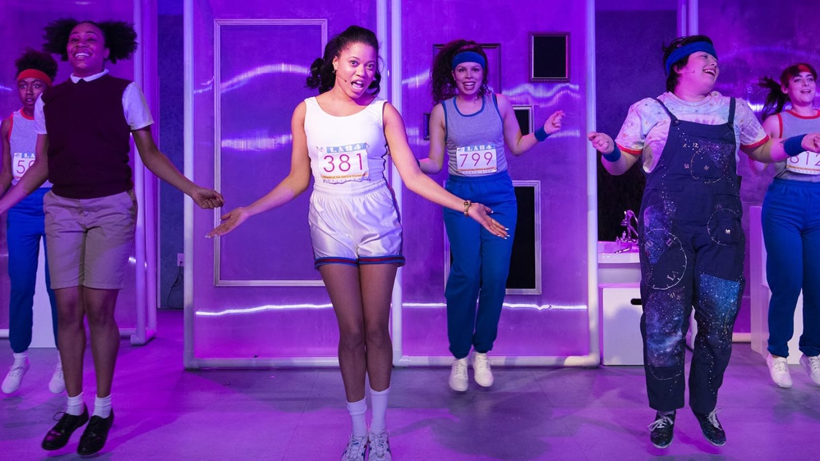 Cast of "She Persisted," the musical, in mid-jump, wearing race bibs.