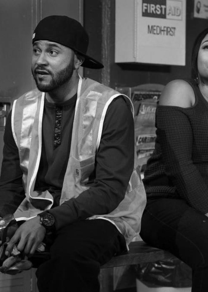 Man and woman seated in a locker room, likely autoworkers in Detroit. "Skeleton Crew" theme.