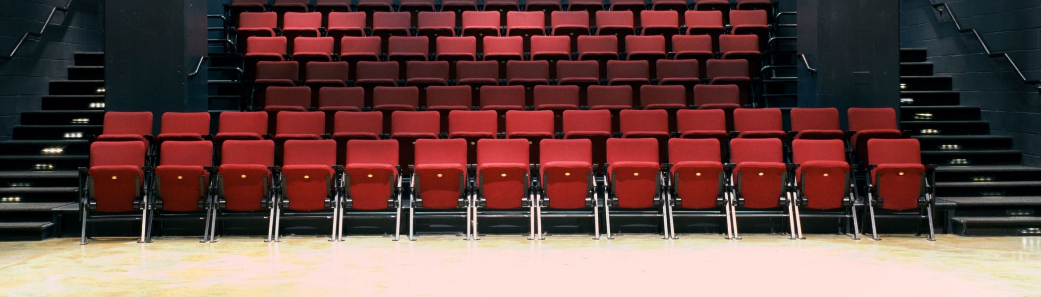 Red theater seats in a rental space, ready for an event. Black walls and stairs.