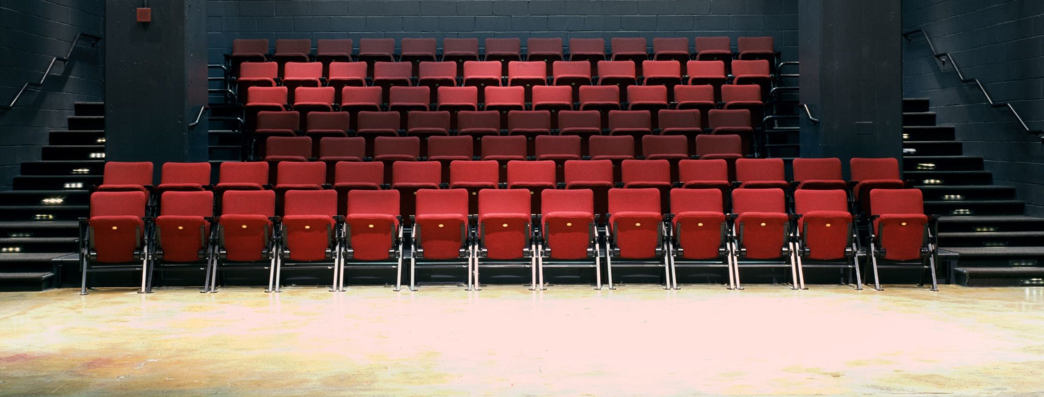 Red theater seats in a rental space, ready for an event. Black walls and stairs.