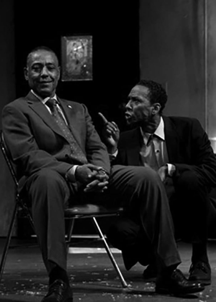 Two actors in "Storefront Church" play. One seated, one speaking intently. Black and white image.