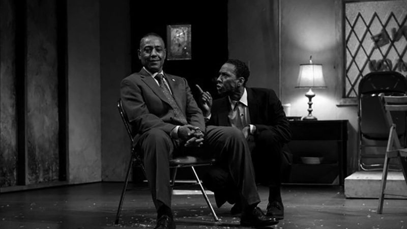 Two actors in "Storefront Church" play. One seated, one speaking intently. Black and white image.