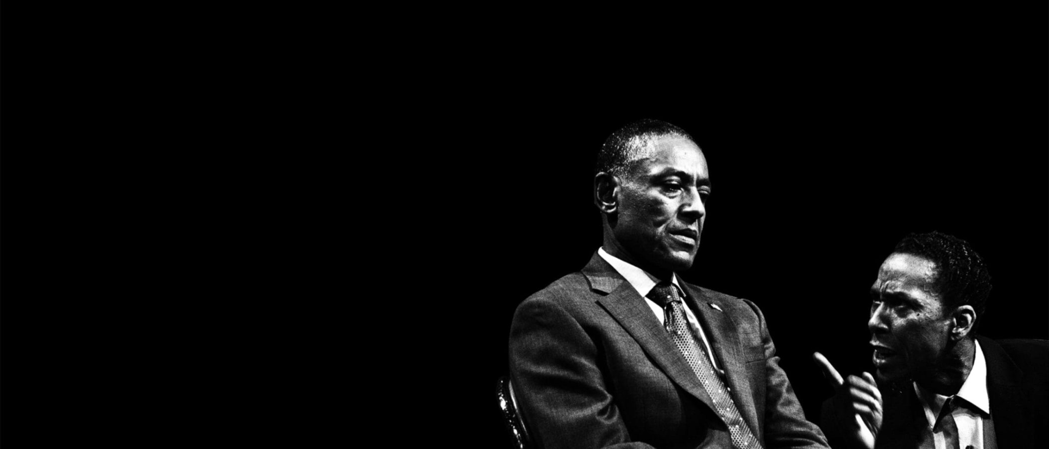 Black and white photo of two men in suits, one appearing pensive, the other gesturing.